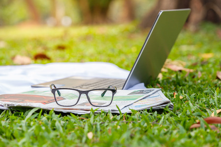 Laptop, newspaper and glasses on the green lawn. select focusの写真素材