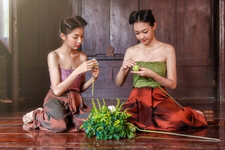 Beautiful Thai girls in thai traditional costume trying to roll up lotus flowerの写真素材