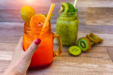 Cropped view image of female left hand holding a healthy fruit with orange juice on the tableの写真素材