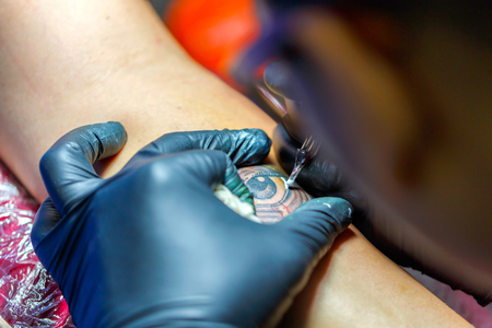 Close up tattoo artist demonstrates the process of getting black tattoo with paint. Master works in black sterile gloves.の写真素材