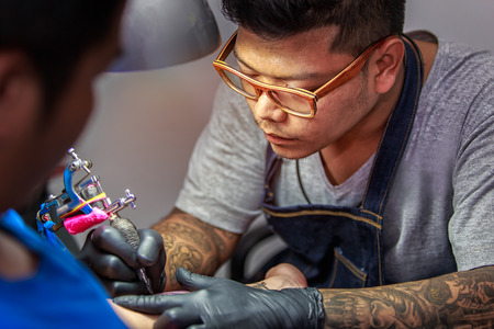 Close up tattoo artist demonstrates the process of getting black tattoo with paint. Master works in black sterile gloves.の写真素材