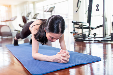 Beautiful young asian woman working out in gym and doing yoga exercise on blue mat.