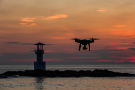 Silhouette of flying drone which taking photo over sunset seaの写真素材