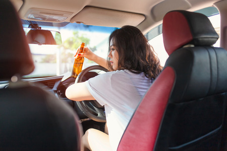 Young asian woman drinking beer while driving a car.の写真素材