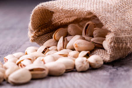 Pistachios nut in burlap sack on grained wood background.の写真素材