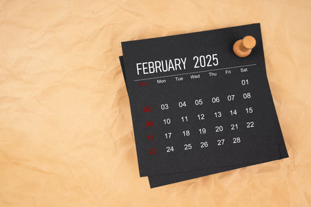 Black calendar sheet for February 2025 with thumbtack on brown paper.の写真素材