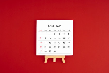 Calendar page for April 2025 with wood easel on a dark red background.の写真素材