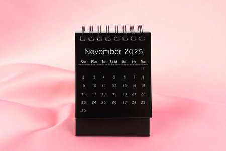 Black desk calendar for November 2025 on a pink color silk textile background.の写真素材