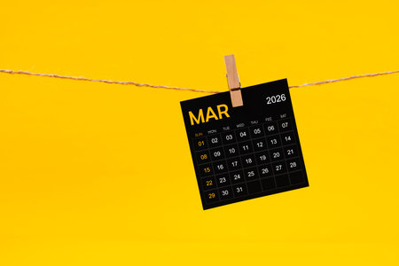 March 2026 black calendar hanged with brown rope on yellow color background.