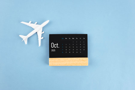 October 2025 black wooden calendar and airplane toy on blue color background.