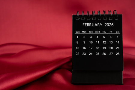 Black desk calendar for February 2026 on a red satin or silk textile background.の写真素材