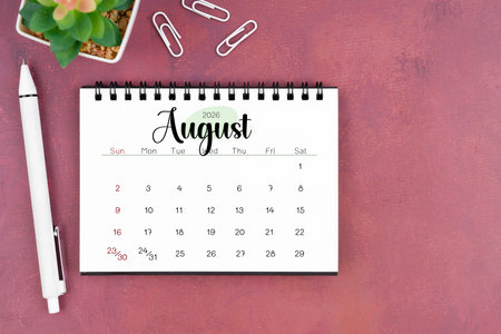 August desk calendar for 2026 year and pen on old red cover.