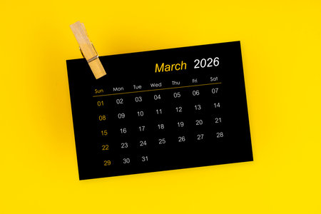 March 2026 black calendar with wooden clip on yellow background.