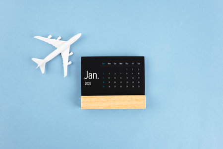 January 2026 black wooden calendar and airplane toy on blue background.