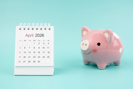 April 2026 Desk calendar and pink piggy bank on blue color background.の写真素材