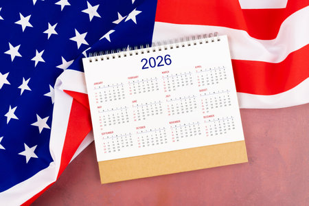 2026 Yearly desk calendar and United States of America flag on red wooden.