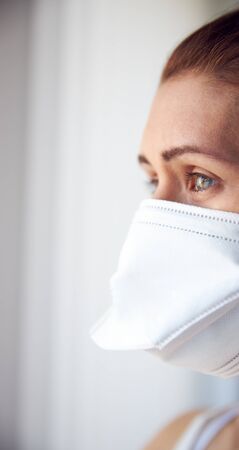 Young woman looking out of window wearing protective face mask with copy space portrait.の写真素材