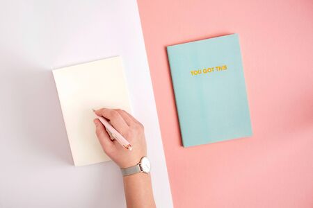 Flat lay of hand writing in notebook on pastel pink and purple.