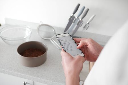 Man looking at recipe on smart phone whilst baking in kitchen.の写真素材