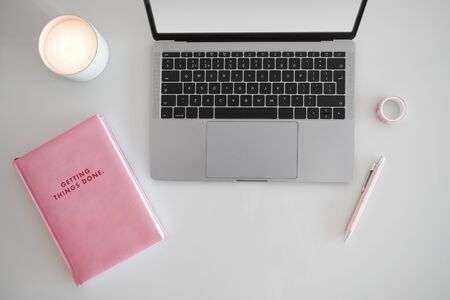 Top view of pink notebook and laptop on white desk.