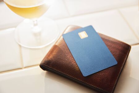 Blank credit card on top of leather wallet on bar next to drink.