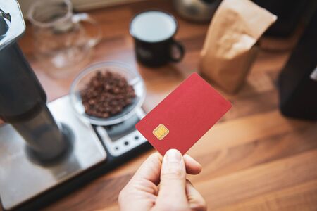Man holding blank red debit card a coffee shop paying for a take out.の写真素材