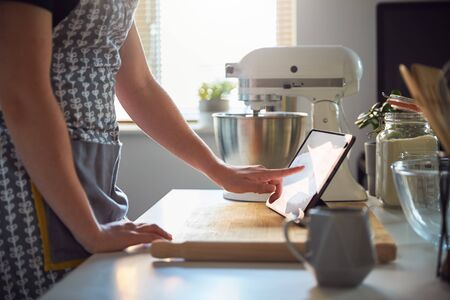 Woman Using Touch Screen on a Digital Tablet In The Kitchen At Home on a Chopping Boardの写真素材