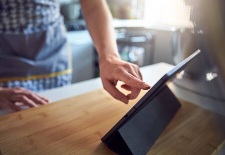 Woman Using Touch Screen on a Digital Tablet In The Kitchen At Home on a Chopping Board