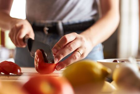 Close-up of woman slicing a tomato on wooden chopping board.