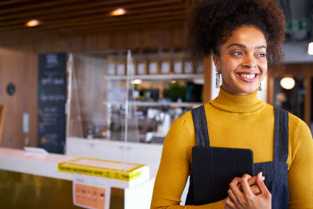 Portrait Of Female Business Owner Of Coffee Shop In Mask Using Digital Tablet During Health Pandemicの写真素材