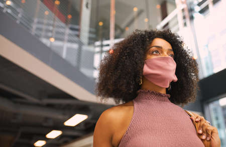 Young Mixed Race Businesswoman Wearing Face Mask In Modern Office Foyer During Covid-19 Pandemicの写真素材