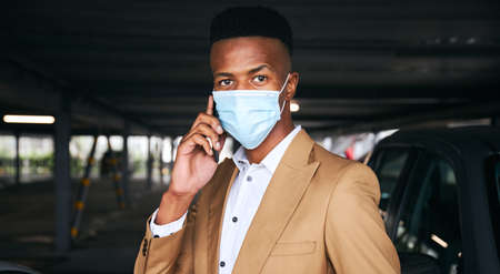Businessman Wearing Mask Using Mobile Phone In Airport Car Park During Health Pandemicの写真素材
