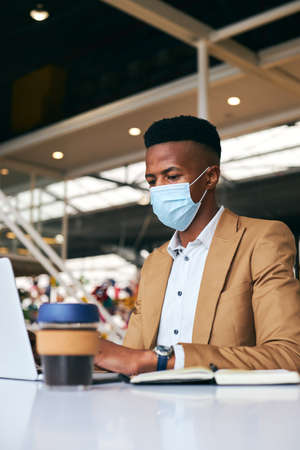 Young Businessman Wearing Mask Working On Laptop At Hot Desk In Office During Health Pandemicの写真素材