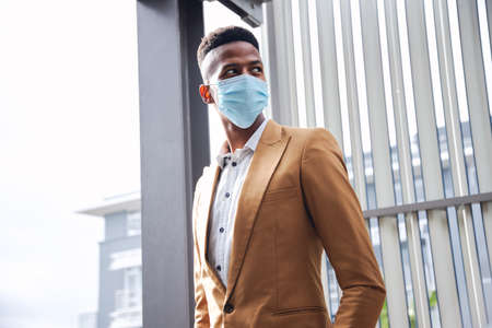 Businessman In Mask Standing Outside Modern Office Building During Health Pandemicの写真素材