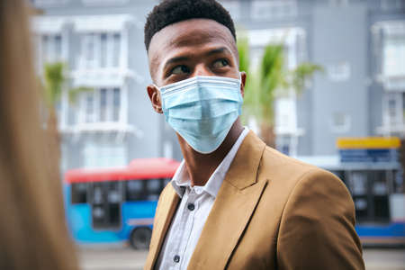 Young Businessman In Mask Standing Outside Modern Office Building During Health Pandemicの写真素材