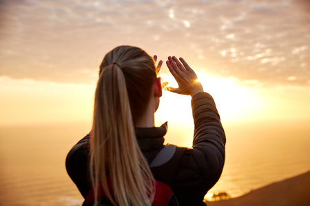 Young woman on vacation wearing backpack walking along coastal path shielding her eyes against the sun reflecting on seaの写真素材