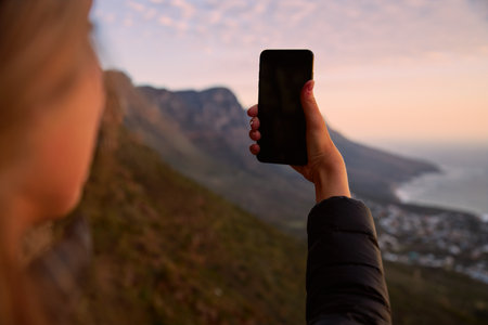 Young woman on vacation walking along coastal path at sunset or sunrise taking selfie to post on social media with mobile phoneの写真素材