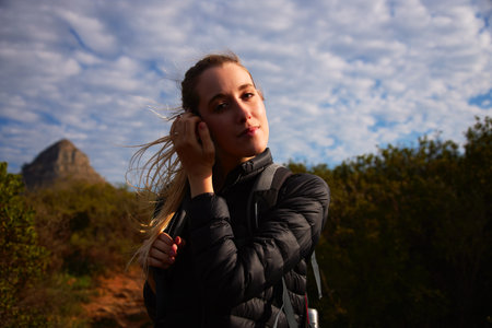 Portrait of young woman on vacation wearing backpack walking along path through countryside on blue...