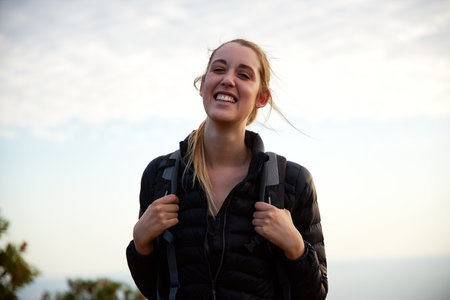 Portrait of young smiling woman on vacation wearing backpack walking along path through countryside...