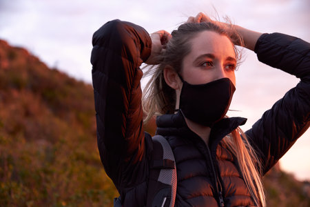 Young woman adjusting face mask on top of mountain during sunset