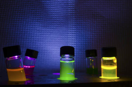 Multiple colourful close up photochemical reaction in glass vial under UV light in a dark chemistry laboratory for biomedical researchの写真素材