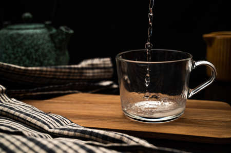 Healthy tea poured into transparent cup. Teapot, lemon, ginger, cardamom, heather bunch and glass jar of daisy teabags and water droplet splash.の写真素材