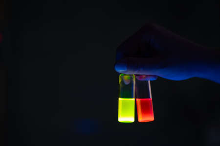 A woman researcher holding chemistry photochemical reaction glass vials in a organic laboratory - radioactive - fluorescence. A copy space black background. Organic medicinal chemistry laboratory.の写真素材