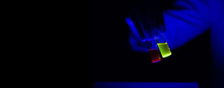 Toxic organic chemical sample glass vials hold by a woman scientist in a laboratory - radioactive - fluorescence. A copy space black background. Organic medicinal chemistry laboratory.の写真素材