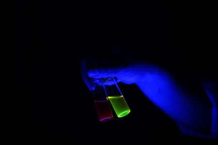 A chemistry woman scientist holding a pair of fluorescent compound solution in small glass vial for biotechnolgy researchの写真素材