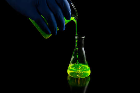 A research scientist experimenting with a green fluorescent droplets in a glass conical flask in dark biomedical laboratory for health care medicine development. Copy space black backgroundの写真素材