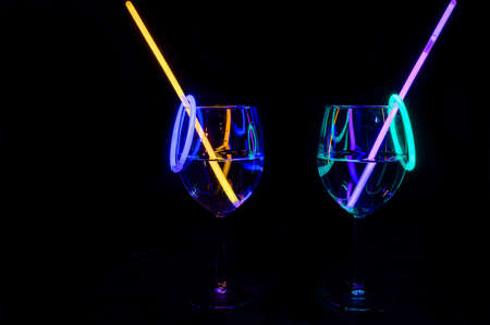 Cocktail wine glass filled with illuminated alcohol liquid and colorful straw with black background for nightlife restaurant docorationの写真素材