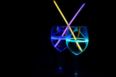 Multicolor mocktail wine glass filled with illuminated relaxing alcohol drink and colorful straw with black background for nightlife party nightclub docorationの写真素材