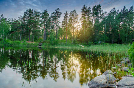 Peaceful tranquill view of dusky evening nature from a lake side with stones in the water during the summer in europe vacationの写真素材