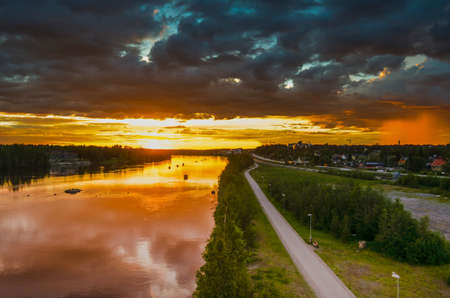 Peaceful reflection of sunlight on moving cloud and local rain on the river through the orange horizon in beautiful summer day in a cityscape backgroundの写真素材